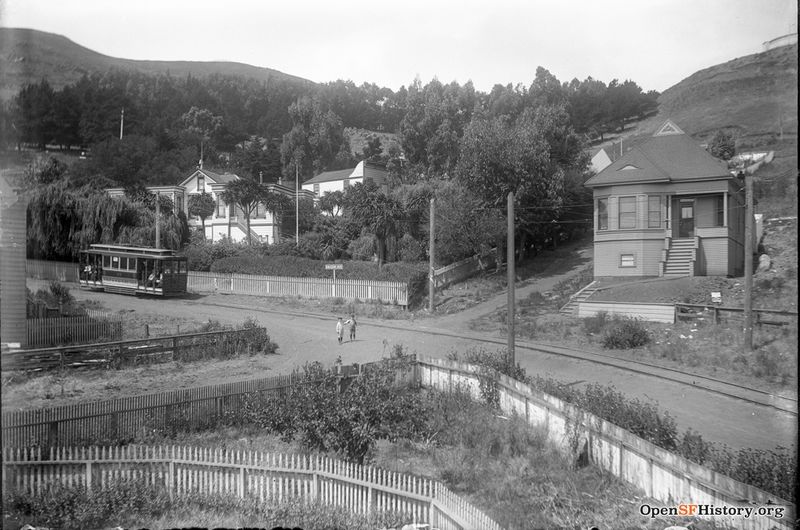 View west toward intersection of Falcon (now Market) and Moss Alley (now 19th). Miller & Joost home (now 3224 Market) at the left. 18th and Park line streetcar, Twin Peaks and Tank Hill in the background wnp15.1723.jpg