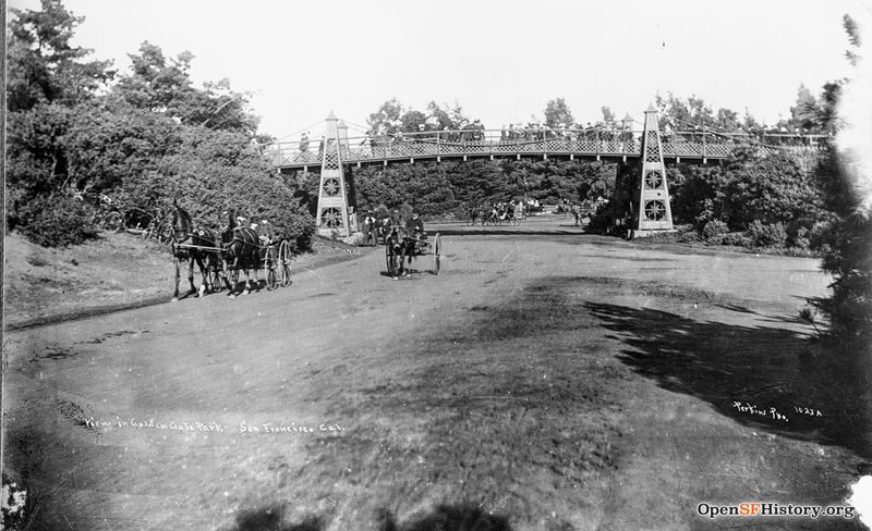 Ggp c 1890 View east on Middle Drive (now Nancy Pelosi) toward steel suspension bridge for pedestrians traveling between the old Bandshell (now Tennis Courts) and Flower Conservatory. Horses and wagons on roadway wnp26.1166.jpg